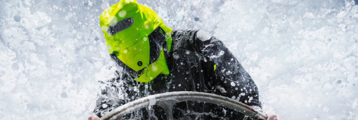 Man at the helm in boat suit with hood in bad weather